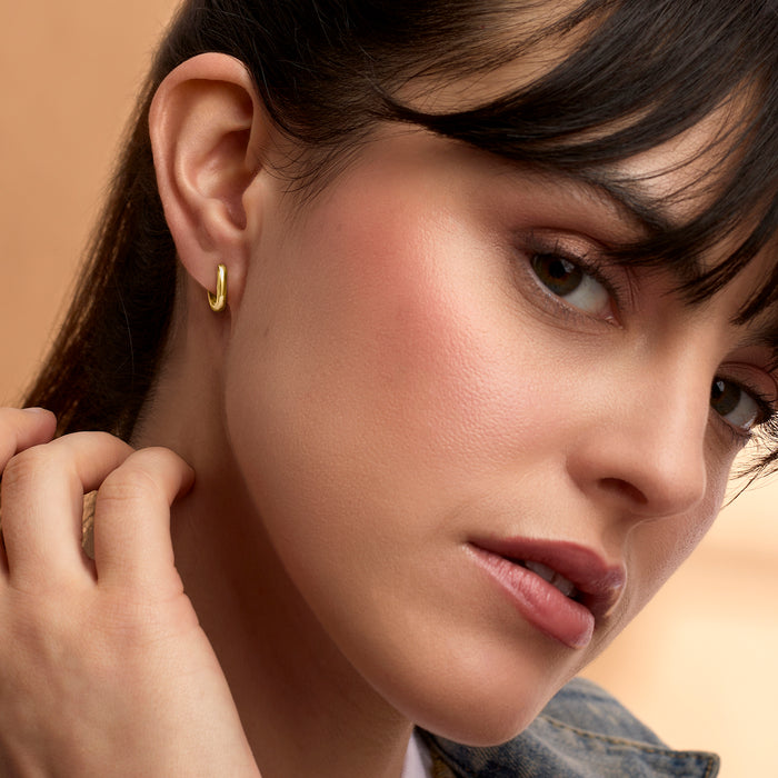 Small yellow gold huggie hoop earrings on ear, oval link hoop design