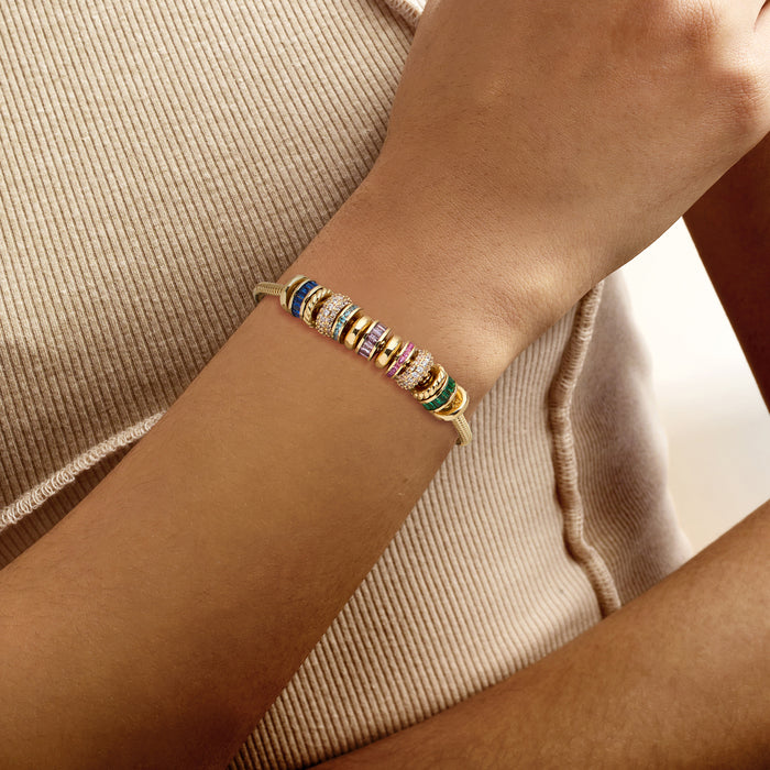 Gold-plated bracelet on wrist with multicolored gemstone cylinder charms and clasp