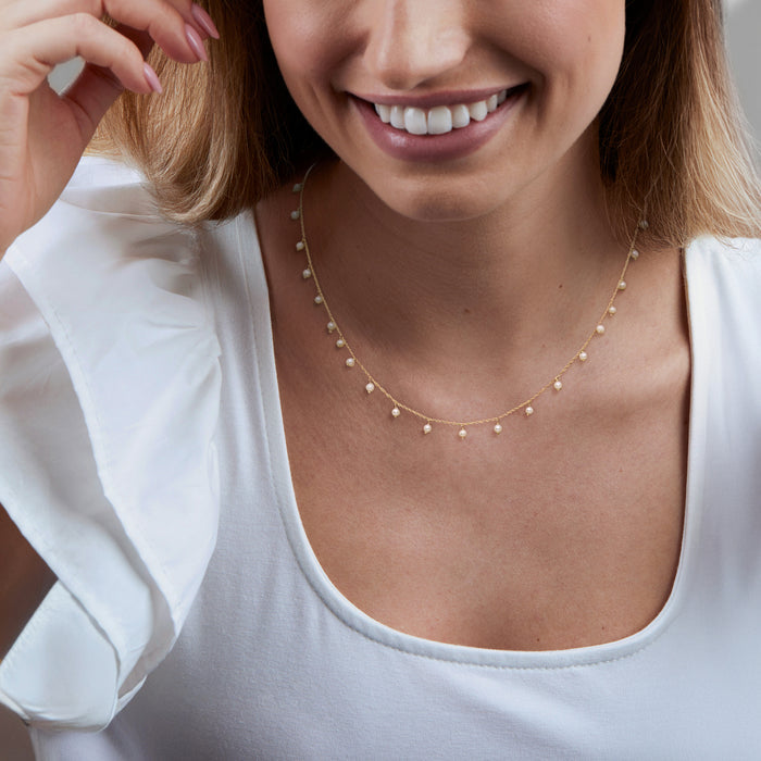 Yellow gold pearl station necklace, small round pearls across collar on model