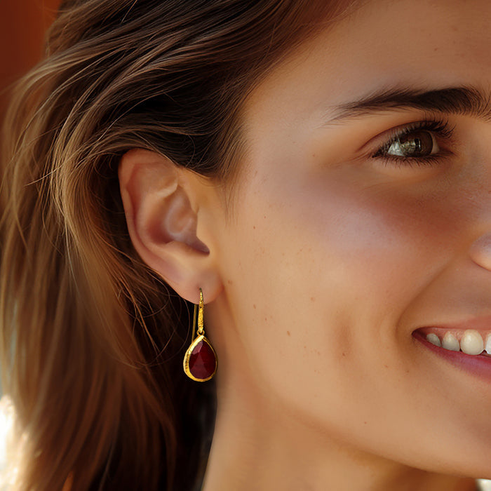 Gold ruby teardrop drop earrings on ear with red gemstone, visible earwire hook