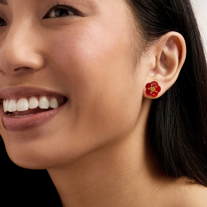 Red flower stud earrings on a model’s ear with gold-tone center details