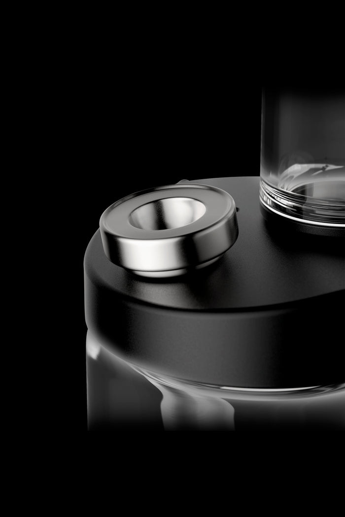 Close-up of a cannabis vape pen's metallic button and glass cartridge against a black background.