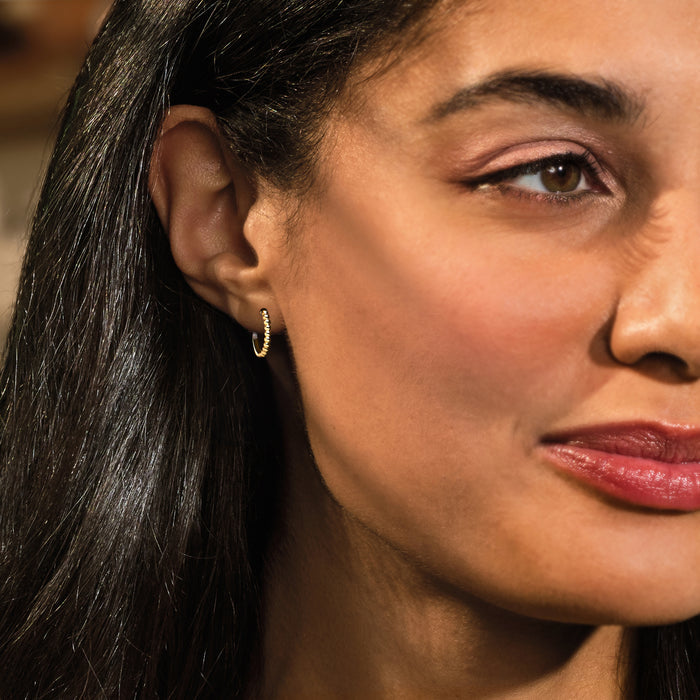 Small yellow gold beaded huggie hoop earrings worn by a woman