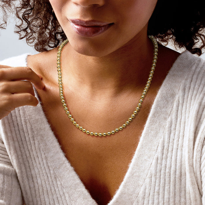 Gold bead necklace worn by model, small round beads with subtle shine.