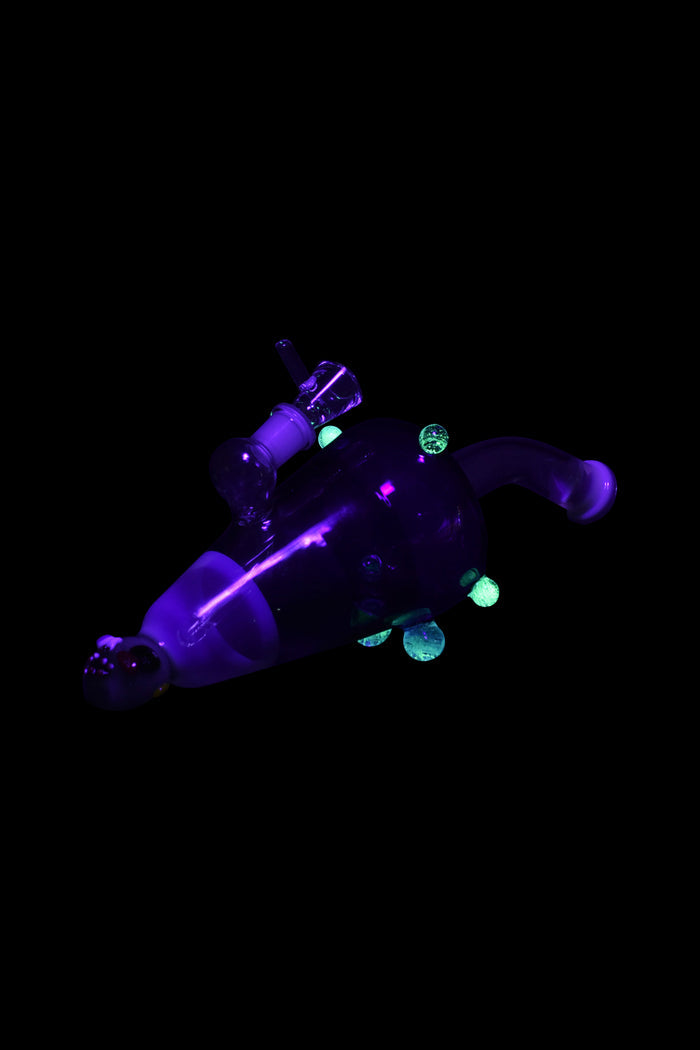 Glowing purple and green glass cannabis water pipe and accompanying pieces floating in darkness.